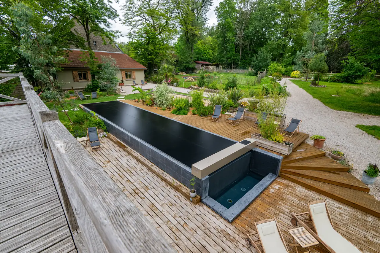Vue en hauteur d’une piscine équipée d’une couverture Coverseal noire, entourée d’une terrasse en bois et d’un jardin paysager